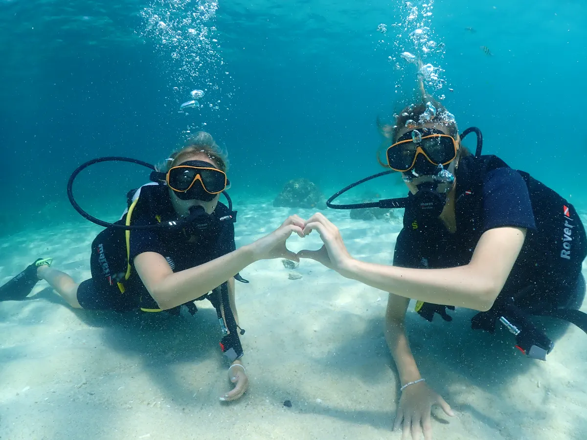 Dos buceadores formando un corazón sobre la arena durante la sesión de habilidades